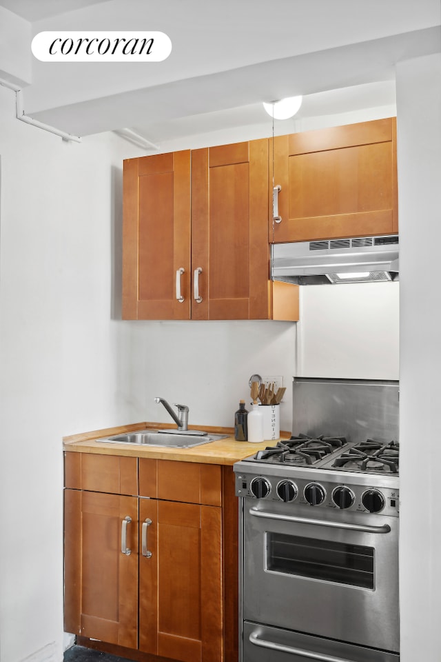 kitchen with a sink, brown cabinetry, under cabinet range hood, and stainless steel gas range oven