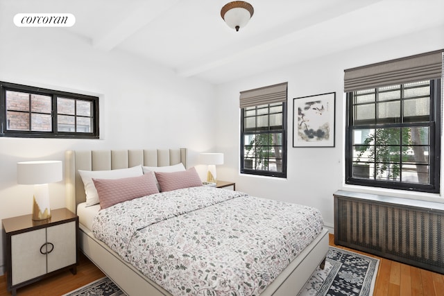 bedroom featuring radiator, beamed ceiling, and wood finished floors