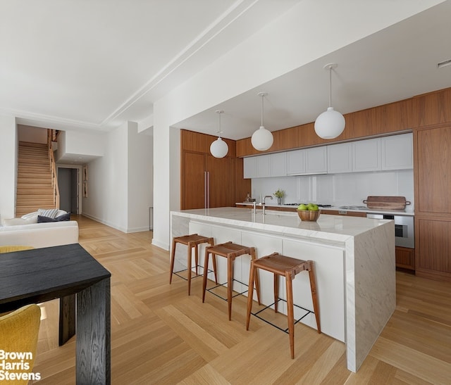 kitchen with brown cabinetry, light stone counters, a breakfast bar area, decorative light fixtures, and a large island with sink