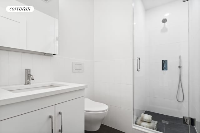 bathroom with vanity, toilet, a shower with shower door, and tile walls