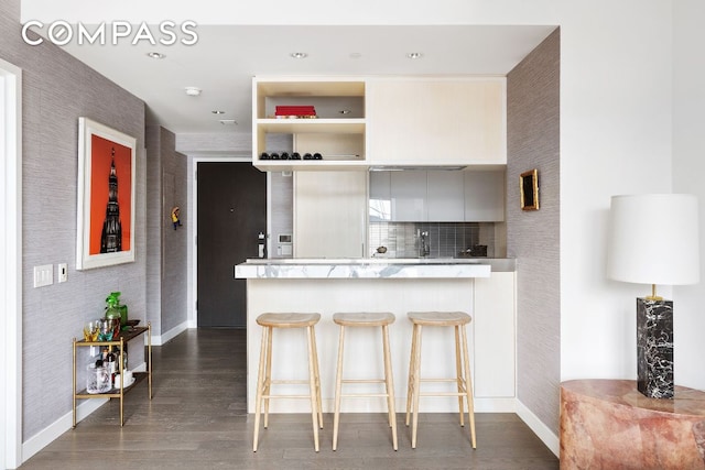 kitchen with a breakfast bar, light countertops, dark wood-type flooring, a peninsula, and wallpapered walls