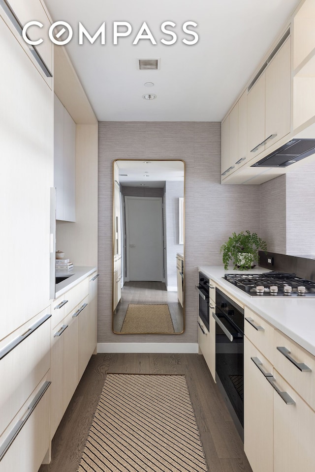 kitchen with wall oven, black oven, stainless steel gas cooktop, dark wood finished floors, and light countertops