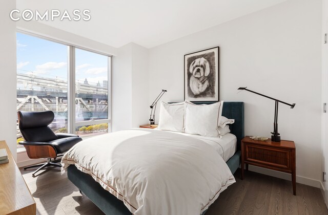 bedroom with baseboards, wood finished floors, and a view of city