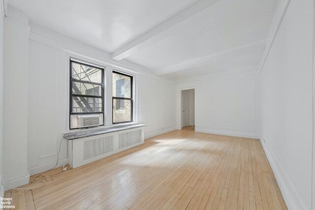 empty room with light hardwood / wood-style floors and beam ceiling