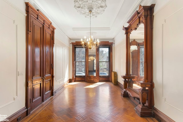 interior space featuring a decorative wall, a notable chandelier, baseboards, and ornamental molding