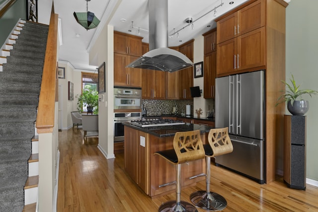 kitchen featuring light hardwood / wood-style flooring, appliances with stainless steel finishes, a kitchen island, island exhaust hood, and decorative backsplash