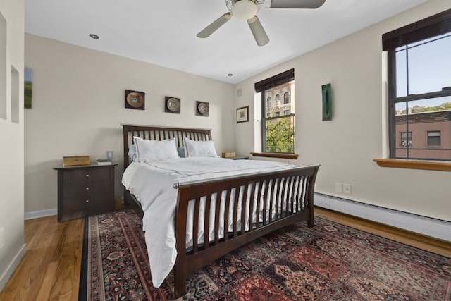 bedroom featuring multiple windows, a baseboard heating unit, hardwood / wood-style flooring, and ceiling fan