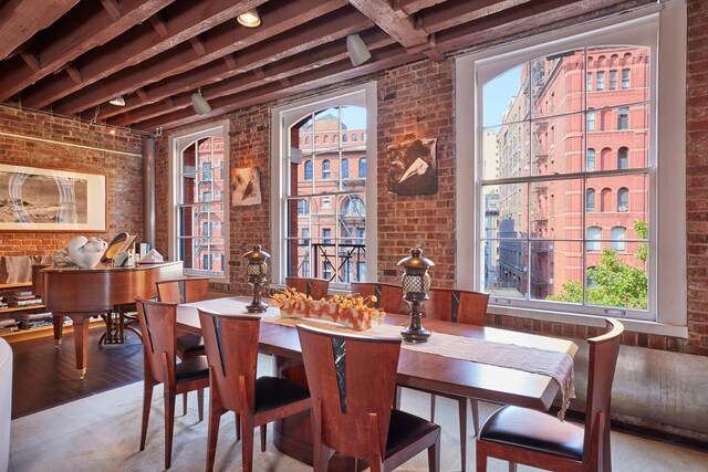 dining space with brick wall, plenty of natural light, wood finished floors, and beam ceiling