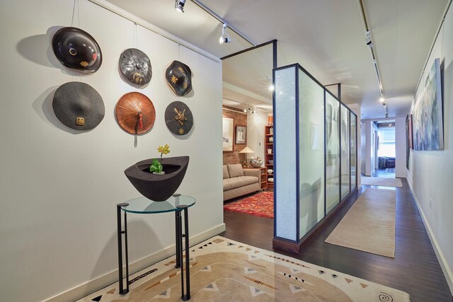 hallway featuring wood finished floors, baseboards, and rail lighting