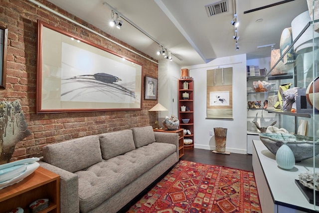 living room featuring dark wood-type flooring, visible vents, brick wall, and track lighting