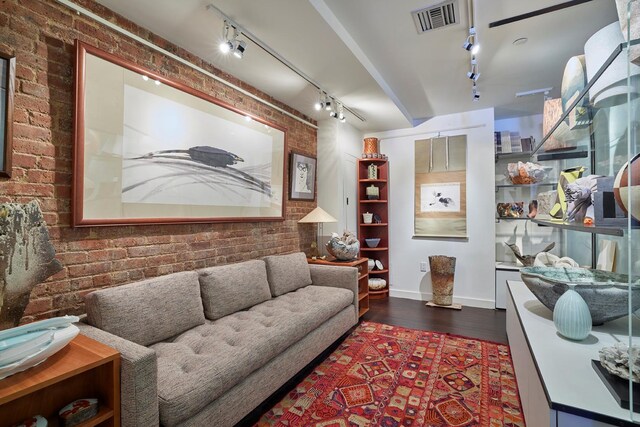 living area with rail lighting, dark wood-style flooring, brick wall, and baseboards