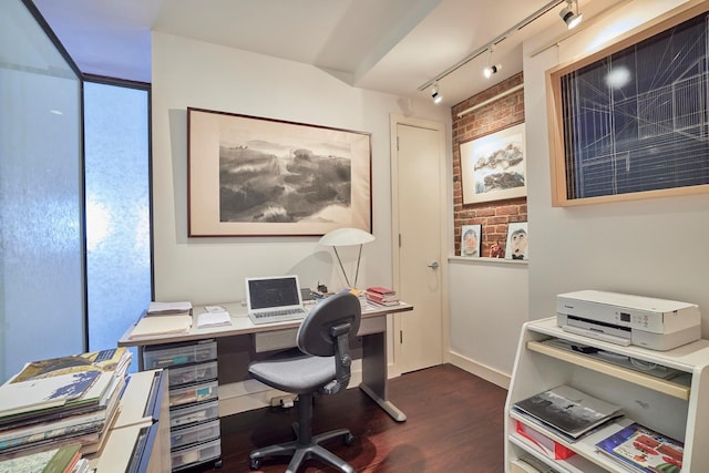 home office with brick wall, dark wood-style floors, and rail lighting