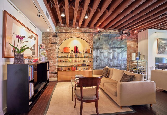 living area with rail lighting, brick wall, hardwood / wood-style floors, and beam ceiling