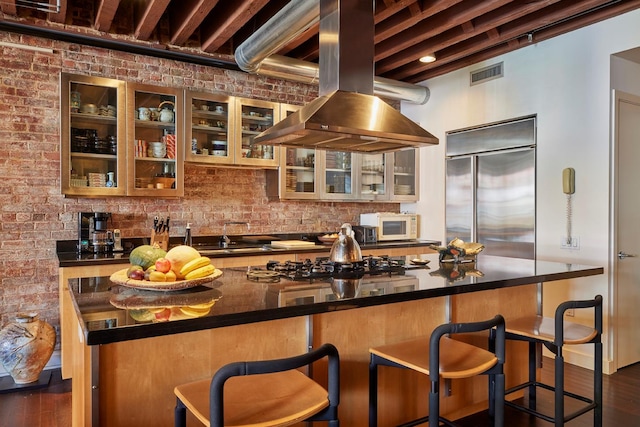 kitchen featuring stainless steel built in fridge, visible vents, dark countertops, island range hood, and white microwave