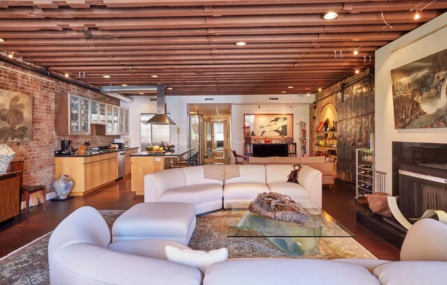 living area with dark wood finished floors, brick wall, and track lighting