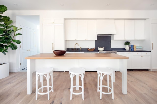 kitchen featuring a sink, light wood-type flooring, custom range hood, and white cabinetry