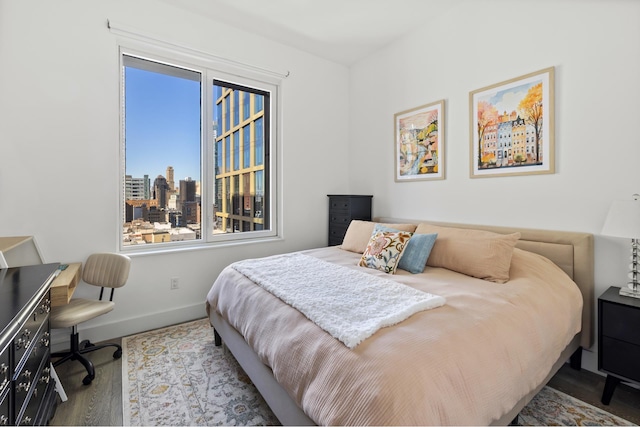bedroom featuring wood finished floors, baseboards, a city view, and a desk
