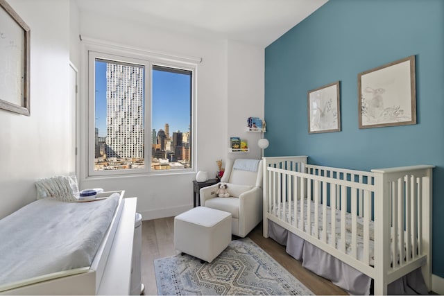 bedroom with wood finished floors, a crib, and baseboards