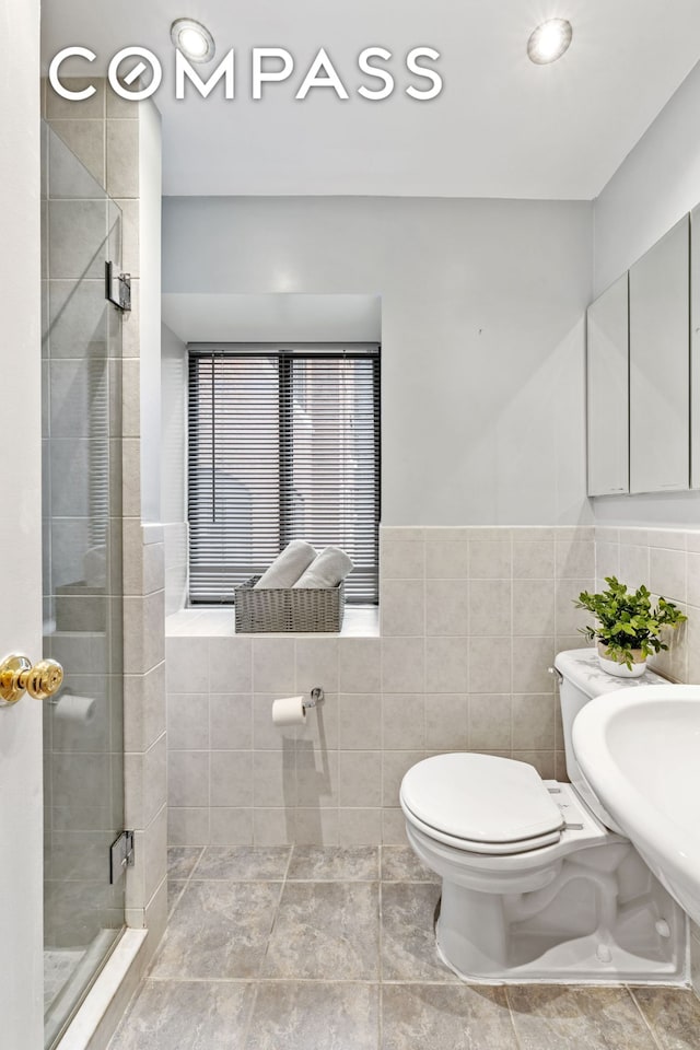 bathroom featuring a stall shower, tile walls, toilet, a wainscoted wall, and a sink