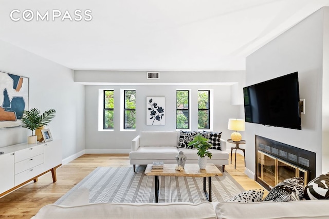 living room with a fireplace with flush hearth, visible vents, light wood-style flooring, and baseboards