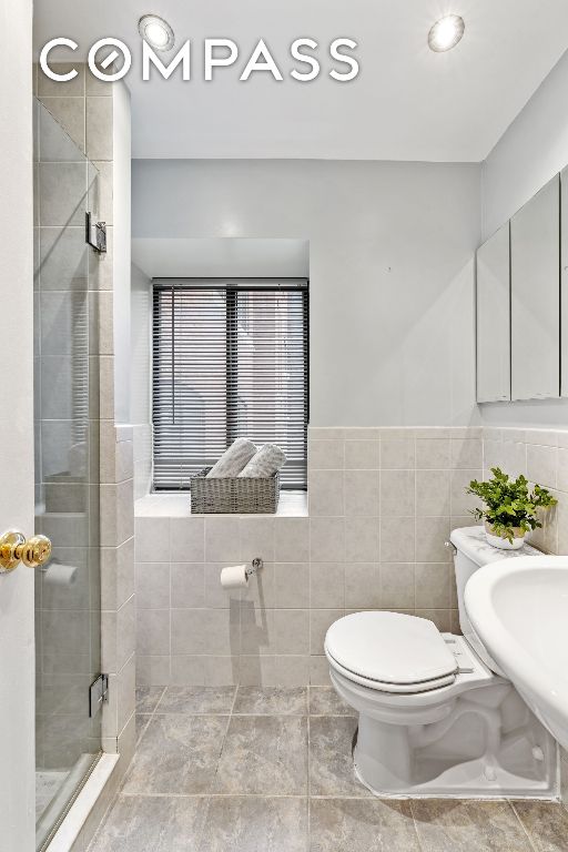 bathroom featuring an enclosed shower, sink, tile walls, and toilet