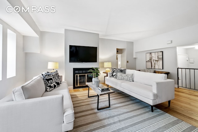 living room featuring light wood finished floors, baseboards, and a glass covered fireplace