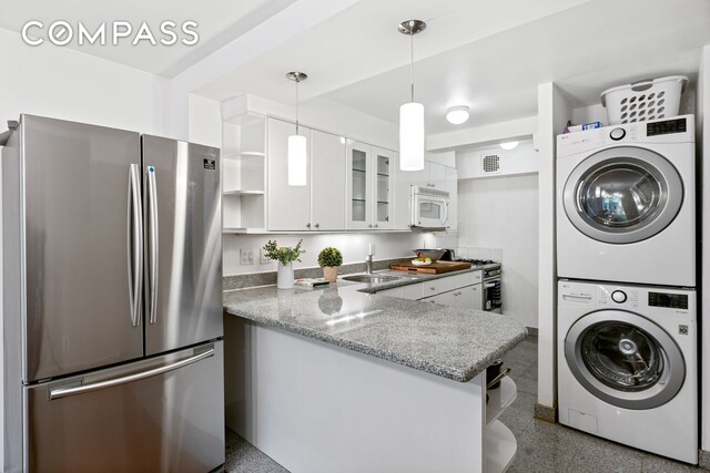 kitchen featuring white microwave, stacked washer and dryer, white cabinets, freestanding refrigerator, and open shelves