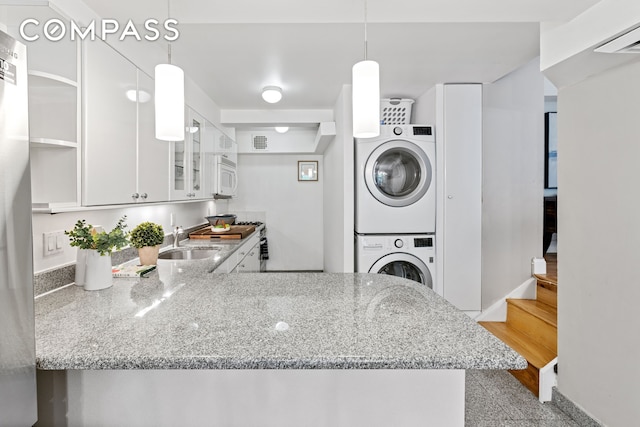 kitchen with light stone counters, stacked washer and dryer, white microwave, white cabinets, and a sink