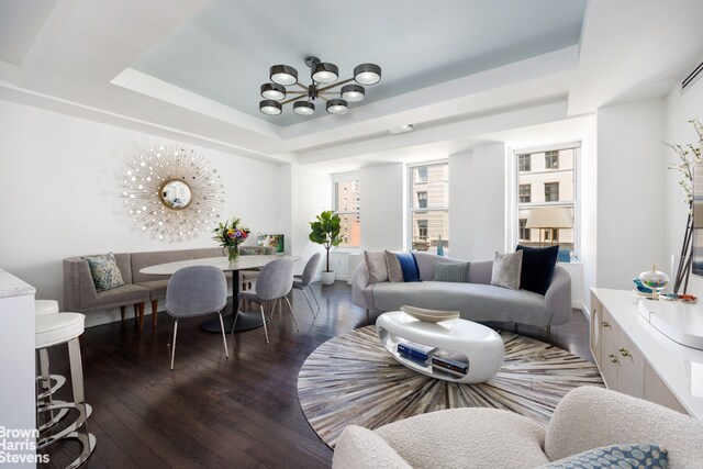 living room with dark wood-type flooring, a chandelier, and a tray ceiling