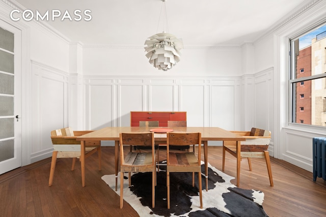 dining space featuring ornamental molding, a chandelier, a decorative wall, and wood finished floors