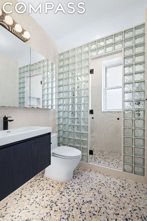 bathroom featuring vanity, tiled shower, tile walls, and toilet