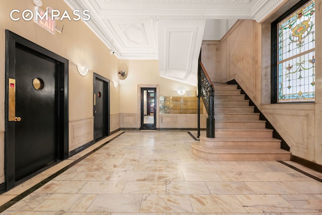 foyer entrance with ornamental molding, inlaid floor details, stairs, and wainscoting