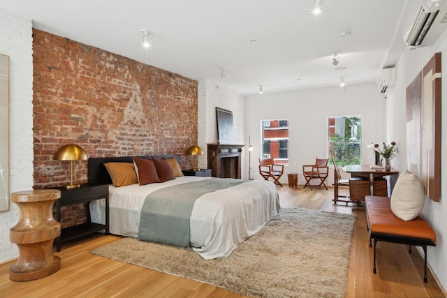 bedroom featuring brick wall, light hardwood / wood-style flooring, and an AC wall unit