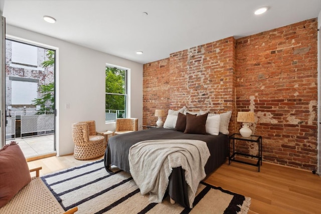 bedroom with brick wall, access to exterior, and light hardwood / wood-style flooring