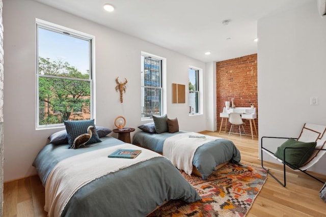 bedroom featuring multiple windows, light hardwood / wood-style flooring, and brick wall