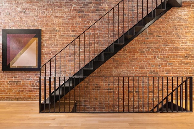 stairway featuring wood-type flooring and brick wall