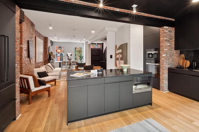 kitchen with brick wall, a large island, double wall oven, and light hardwood / wood-style flooring