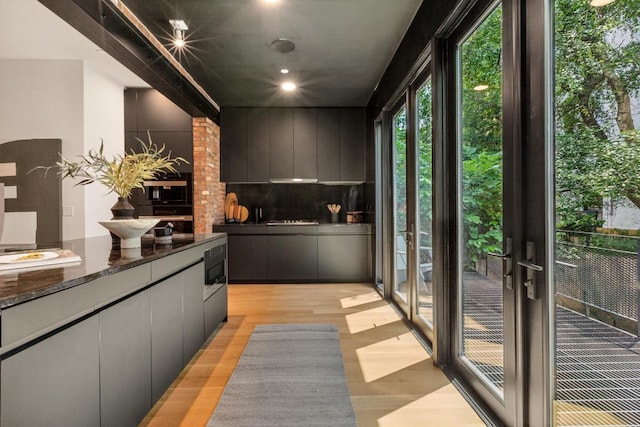 interior space with tasteful backsplash, built in microwave, light hardwood / wood-style flooring, and dark stone countertops