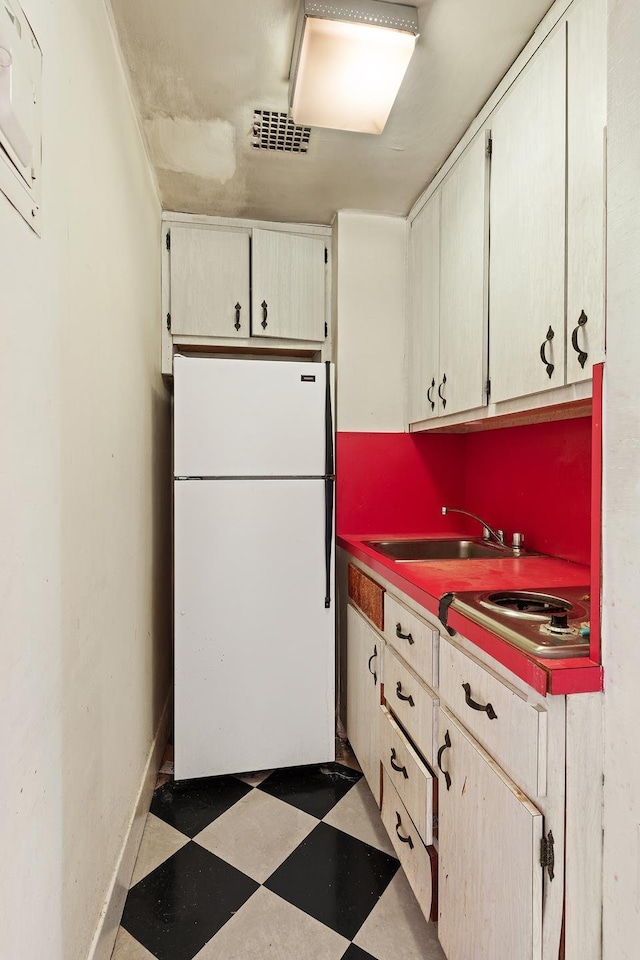 kitchen featuring visible vents, freestanding refrigerator, a sink, baseboards, and tile patterned floors