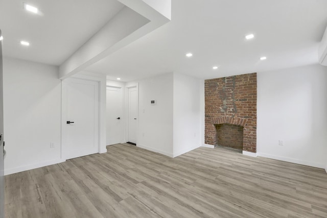 finished below grade area with a brick fireplace, recessed lighting, baseboards, and light wood finished floors