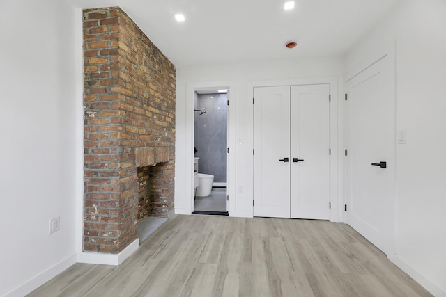 unfurnished bedroom with baseboards, ensuite bathroom, wood finished floors, and a closet