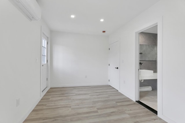 unfurnished bedroom featuring baseboards, a wall mounted AC, ensuite bath, recessed lighting, and light wood-style floors