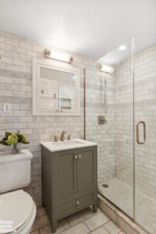 bathroom featuring tile patterned floors, toilet, an enclosed shower, tile walls, and vanity