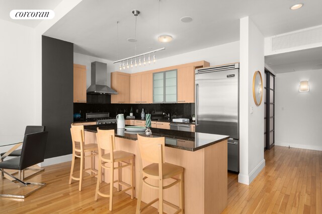 kitchen featuring built in fridge, a kitchen island, decorative backsplash, light brown cabinets, and wall chimney exhaust hood