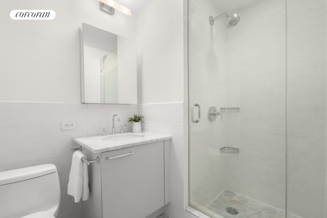 bathroom featuring vanity, toilet, a shower with door, and tile walls