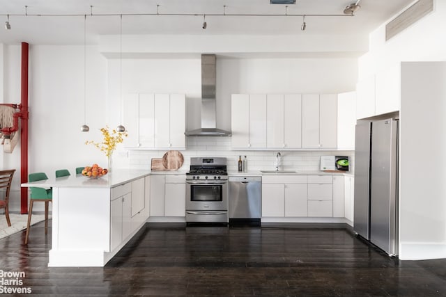 kitchen featuring a sink, wall chimney range hood, light countertops, appliances with stainless steel finishes, and a peninsula