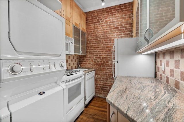 kitchen featuring brick wall, light stone counters, stacked washer and clothes dryer, white appliances, and dark wood-style flooring