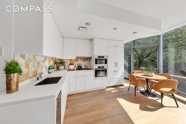 kitchen featuring light wood-type flooring, tasteful backsplash, modern cabinets, and a sink