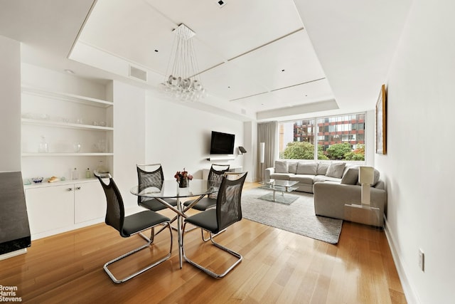 dining room with light hardwood / wood-style floors, built in features, and a notable chandelier