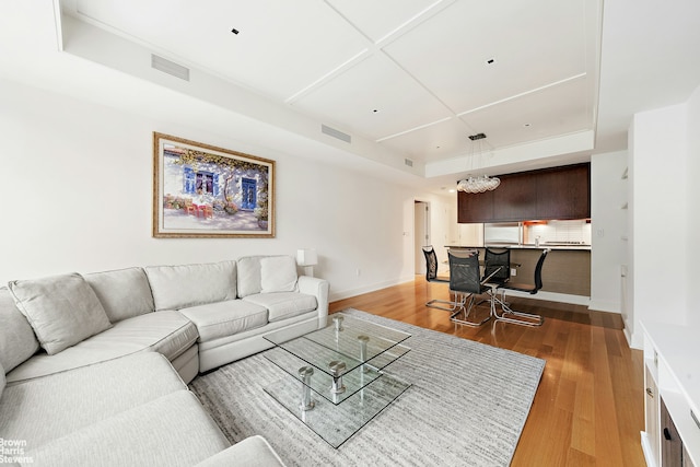 living area with wood finished floors, baseboards, a raised ceiling, and a chandelier